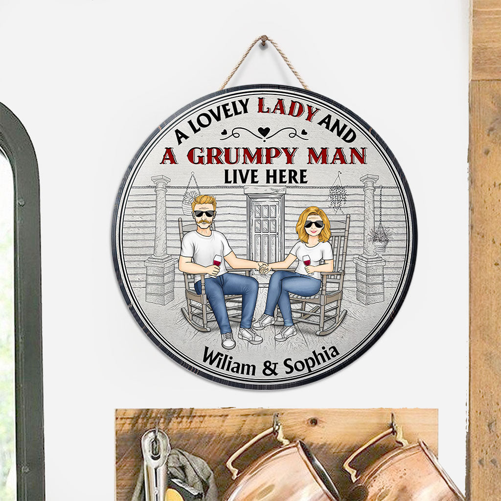 Hier wohnen eine reizende Dame und ein mürrischer alter Mann – personalisiertes rundes Holzschild für Paare